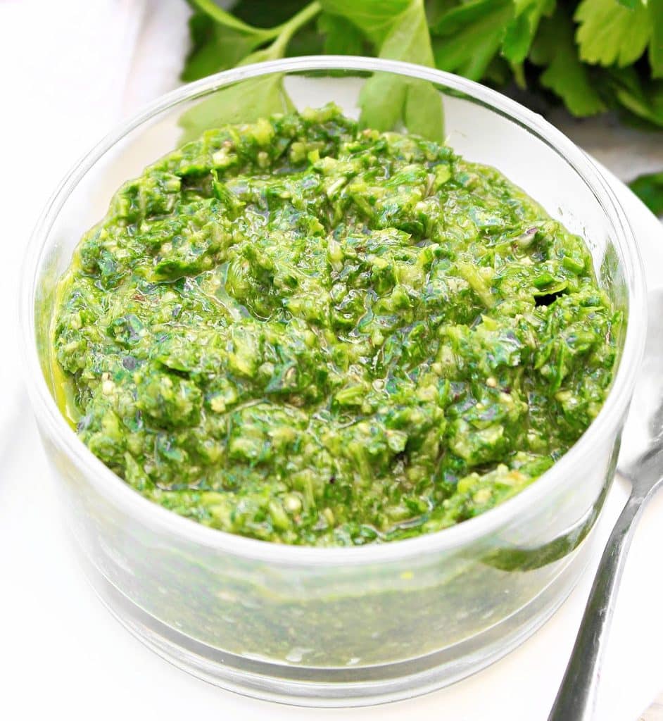 A bowl of herbaceous green chimichurri sauce with a spoon.