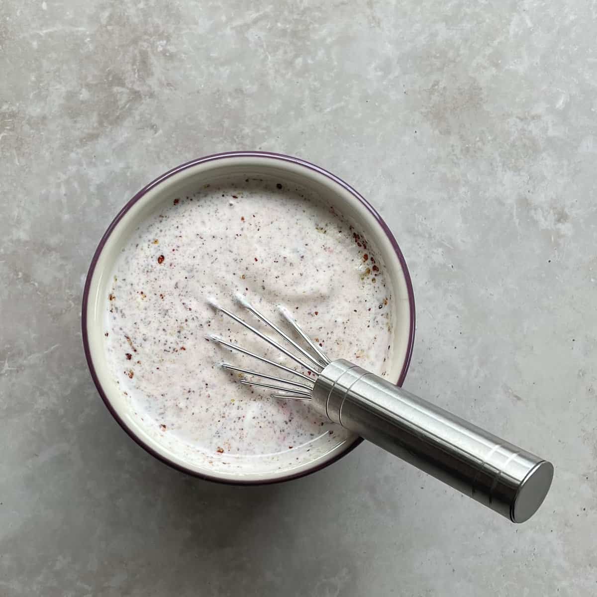 A bowl of sumac dressing with whisk.