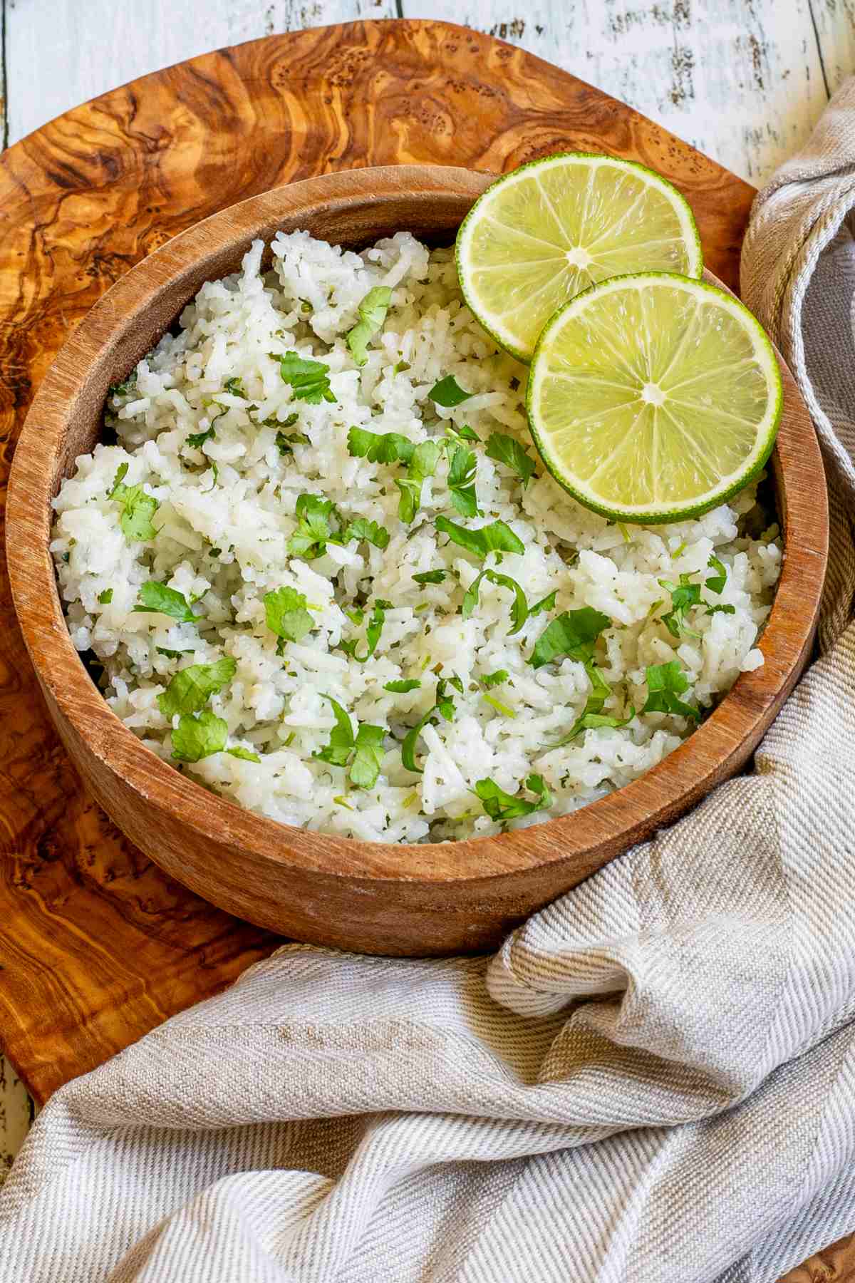 White rice with chopped cilantro and lime slices in a wooden bowl.