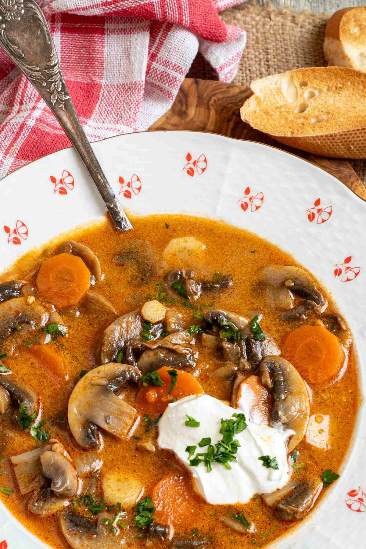 Closeup shot of a bowl of Hungarian mushroom soup with sour cream on a wooden cutting board.