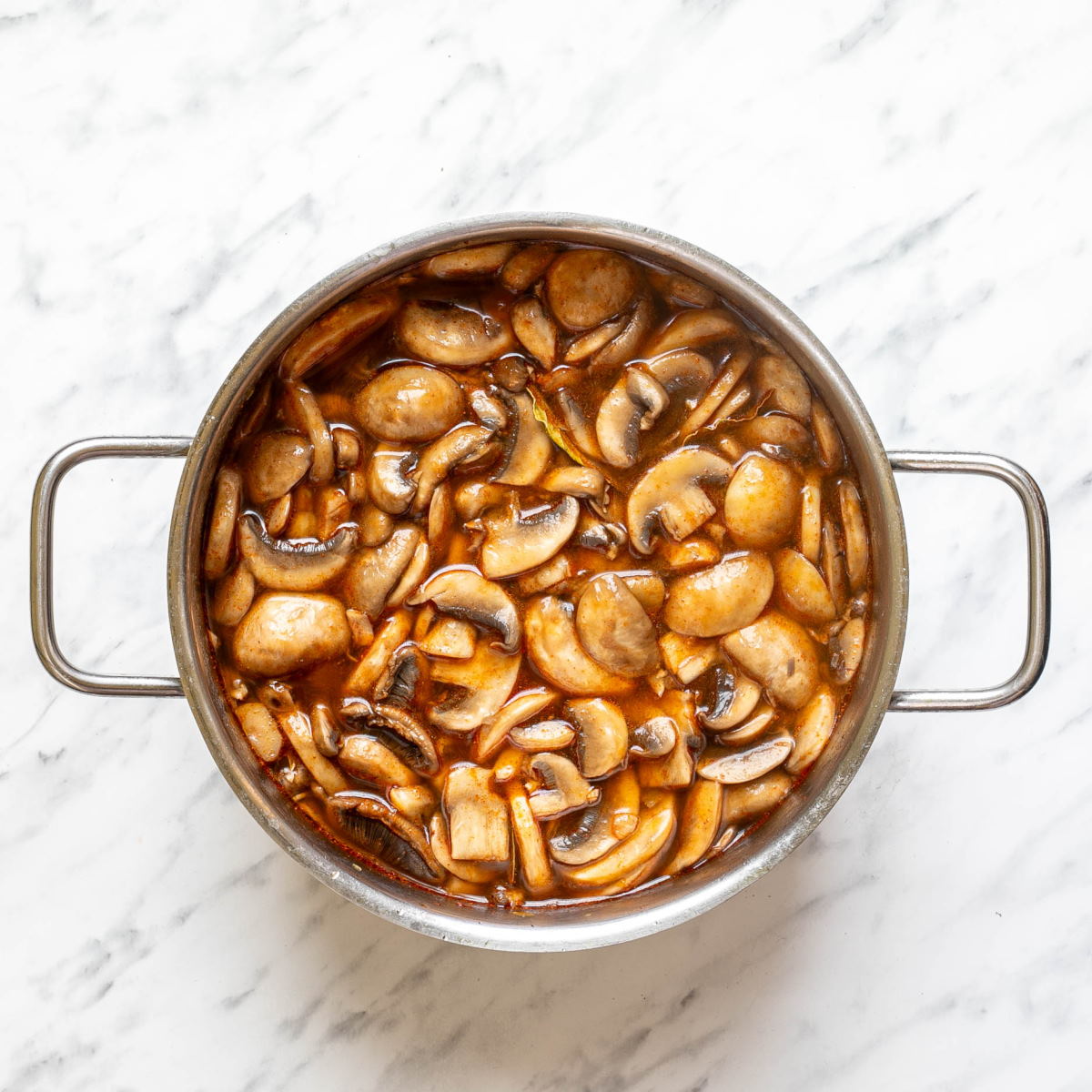 Vegetable broth in a stock pot with sauteed mushrooms and veggies to make Hungarian mushroom soup.