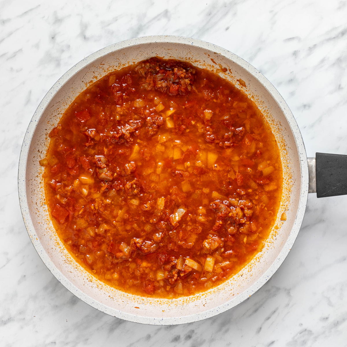 Liquid in a pan with a tomato, spices, and vegetable mixture.