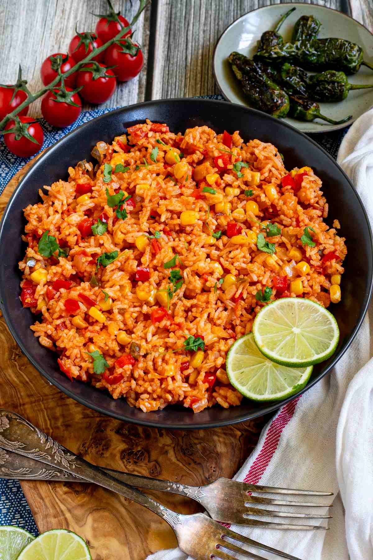 Orange rice with corn, tomato, and parsley in a black bowl. Lime slices are on the side.