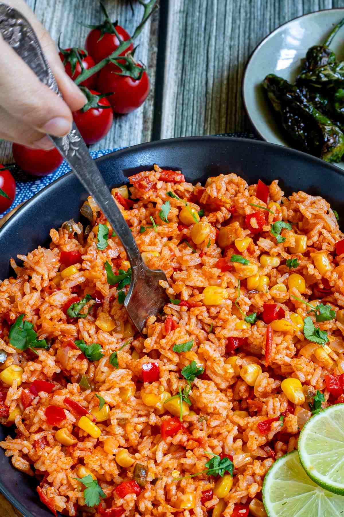 Orange rice with corn, tomato, and parsley in a black bowl. A hand is holding a fork and placed in the middle.