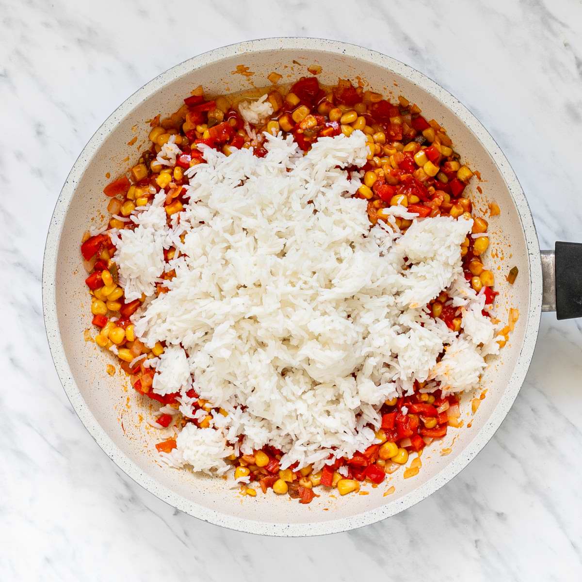 White frying pan with a mix of chopped tomatoes, bell peppers, corn and olives topped with white rice.