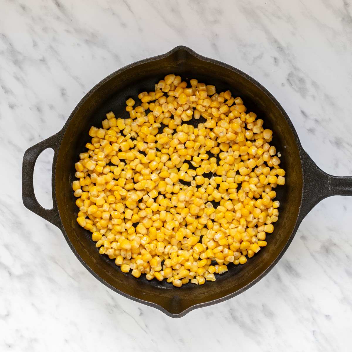 Cast iron skillet full of yellow corn kernels. 