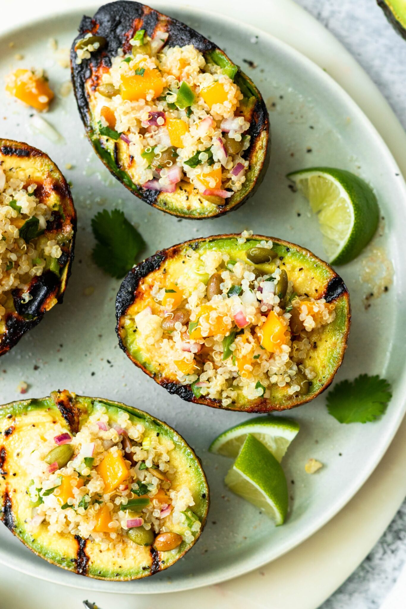 Quinoa stuffed grilled avocados on a plate with lime wedges on the side.