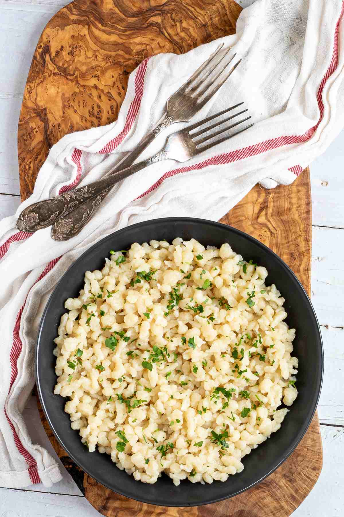 Black plate with small dumplings, in Hungarian nokedli sprinkled with freshly chopped green herbs.