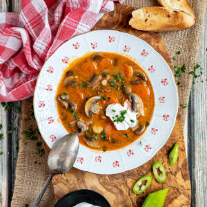 A bowl of Hungarian mushroom soup with sour cream on a wooden cutting board.