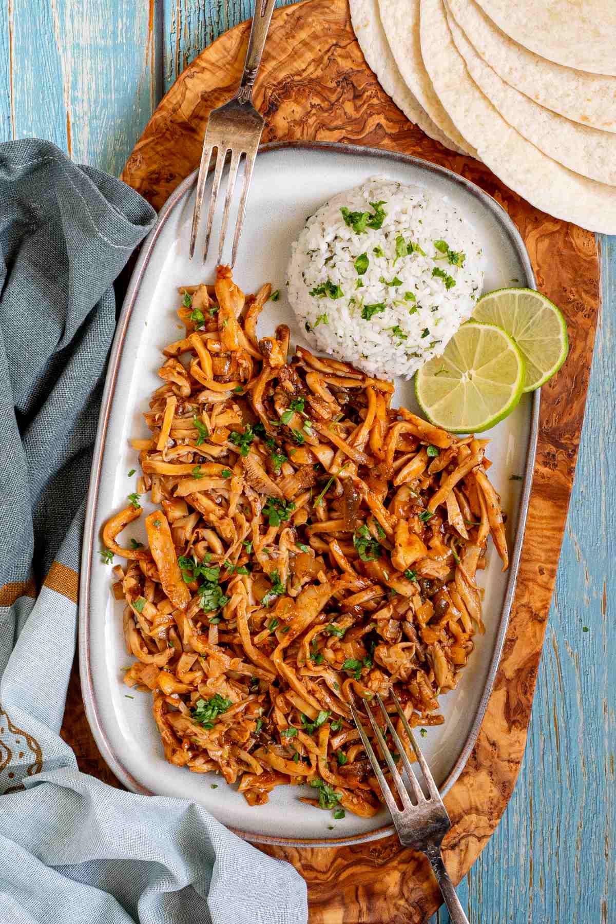 Thin juicy golden brown oyster mushrooms shred sprinkled with chopped green herbs on a light blue tray served with a scoop of rice.