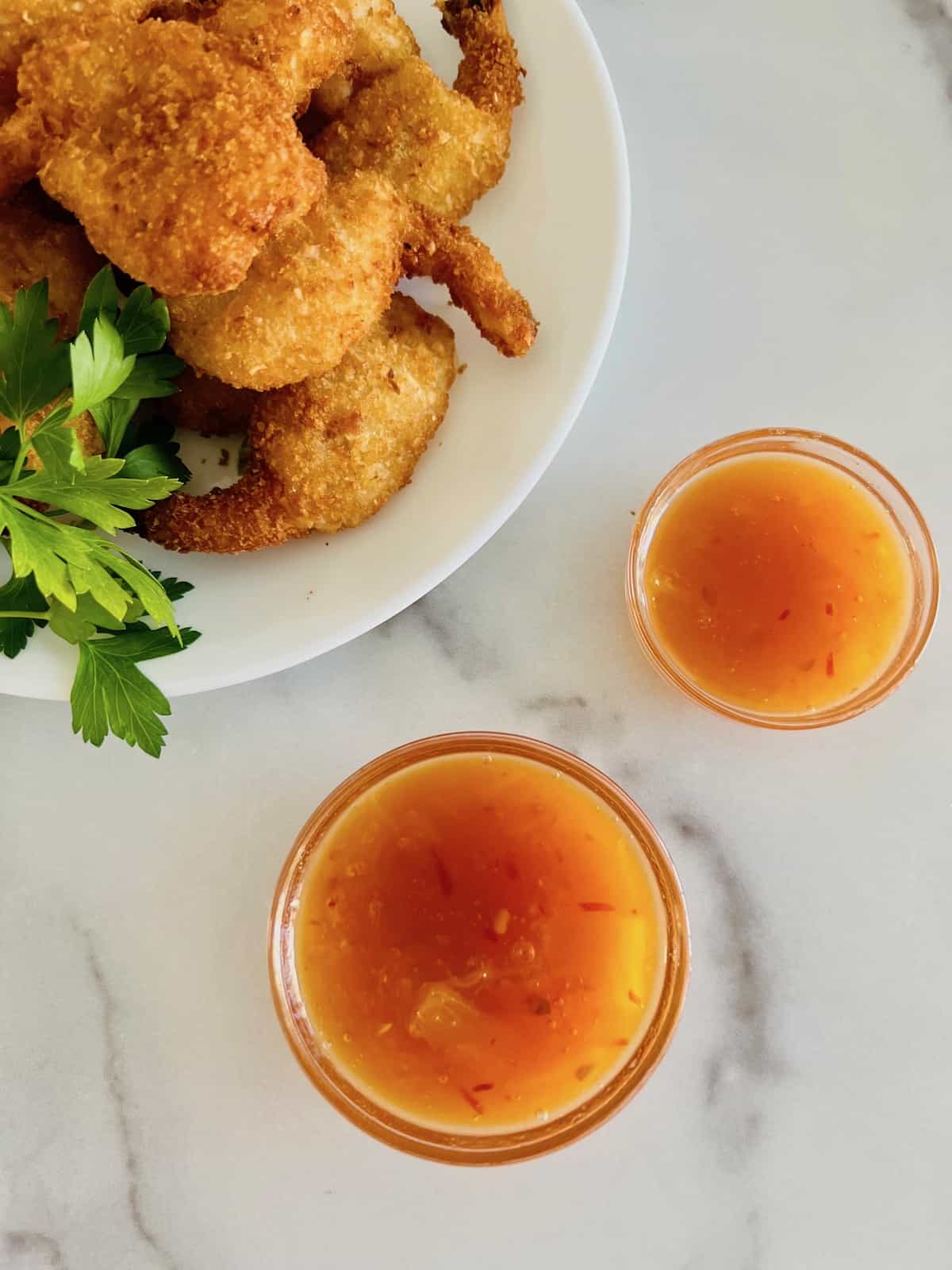 Two glass bowls filled wtih pineapple dipping sauce next to a plate of coconut shrimp. 
