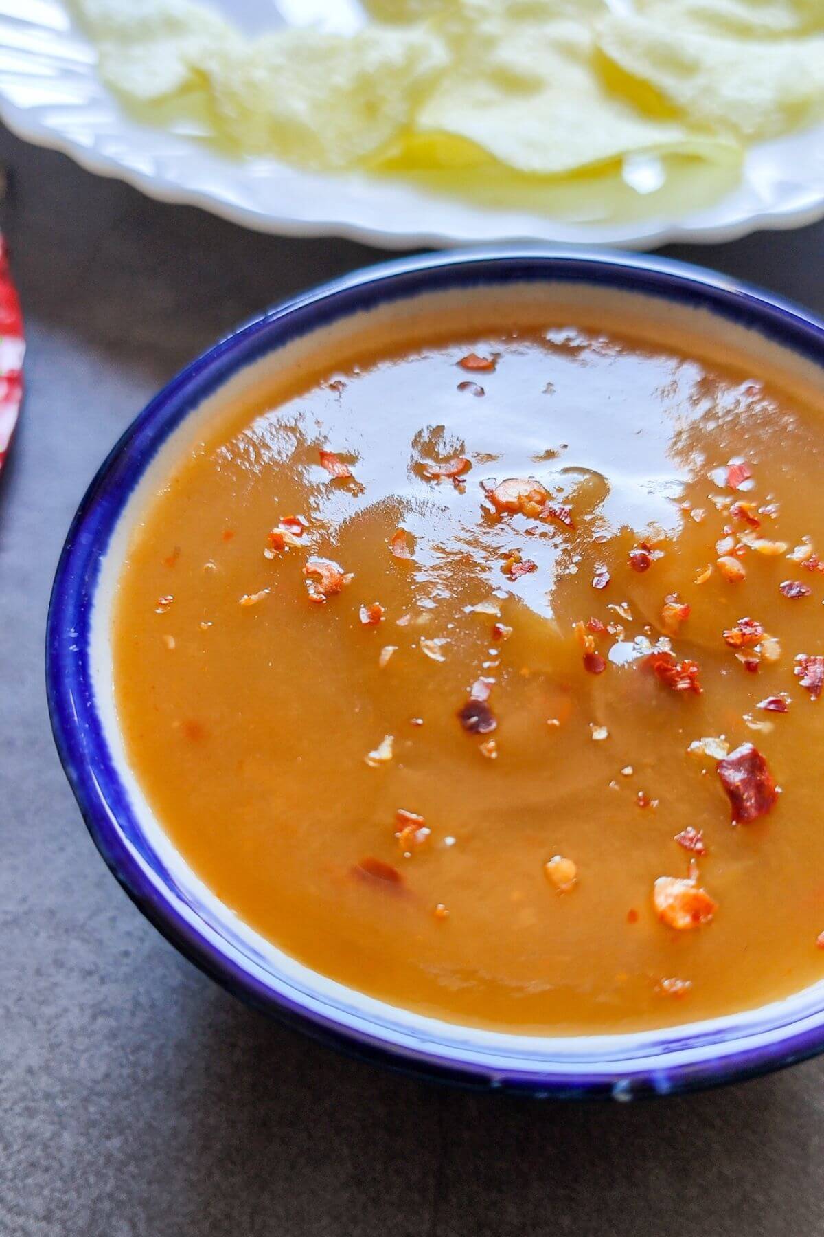 Sweet mango chili sauce served in a bowl with potato chips in the background.
