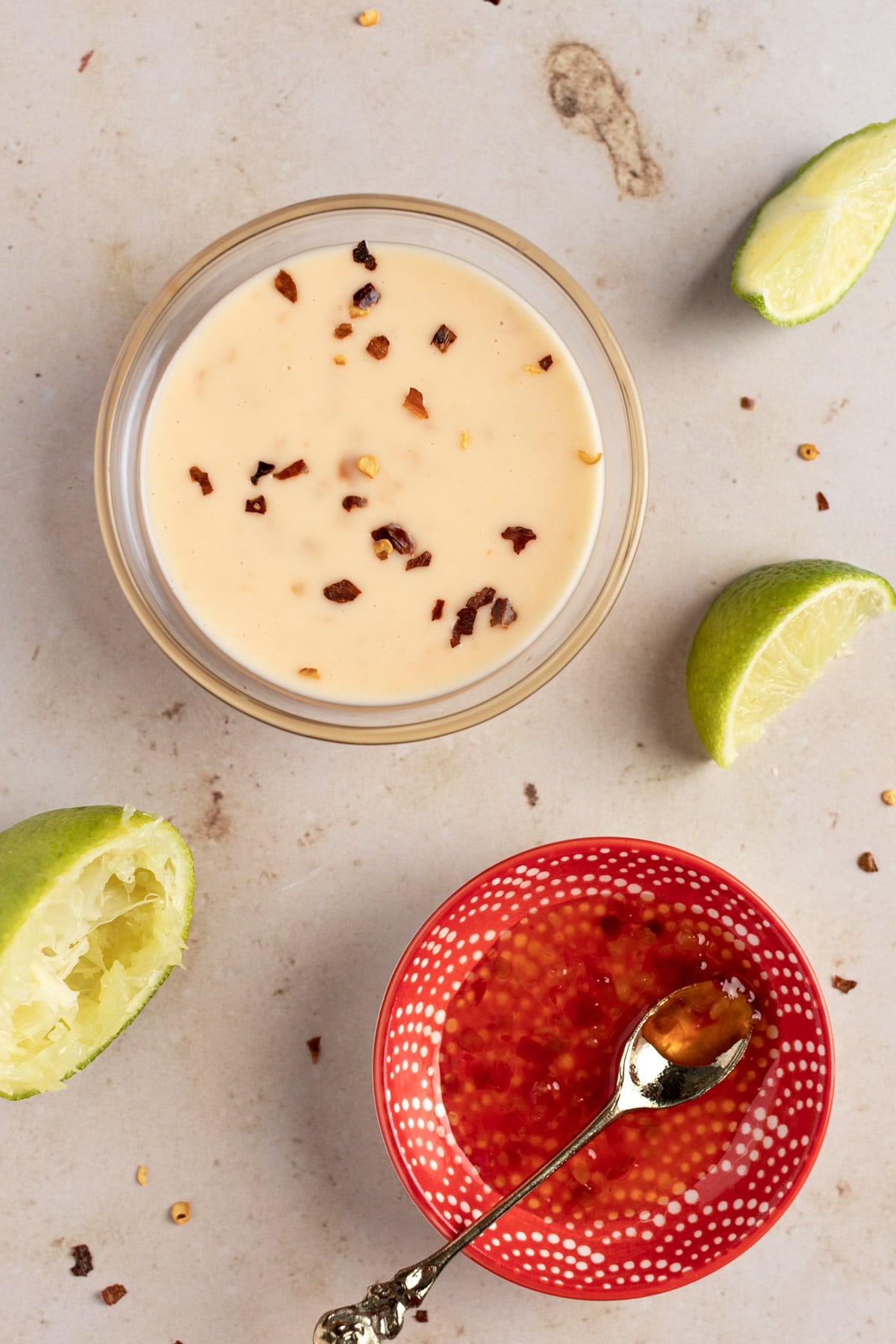 Sweet chili aioli dipping sauce, on a table next to lime slices and sweet chili sauce. 
