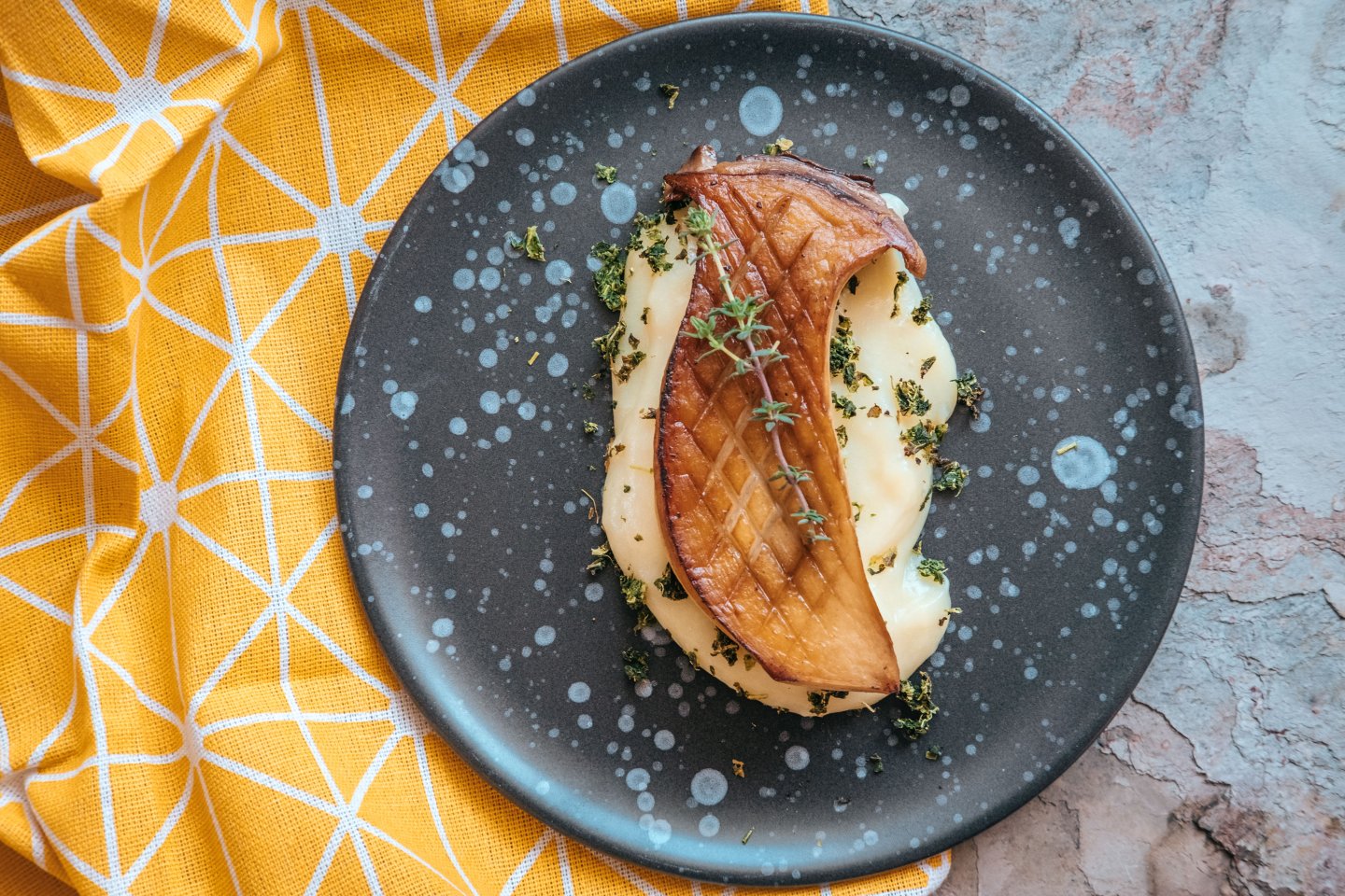 A slice of dark brown grilled king oyster mushrooms on top of a yellow mash served on a black plate.